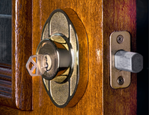 A gold deadbolt with a gold key in it. The deadbolt is installed on a medium brown door that is open